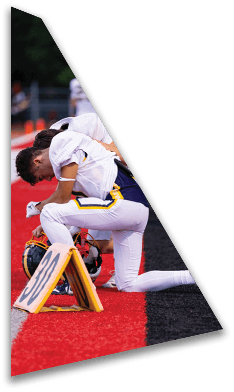 Two people in white football uniforms kneel on a red and black field near a down marker. Description generated by AI