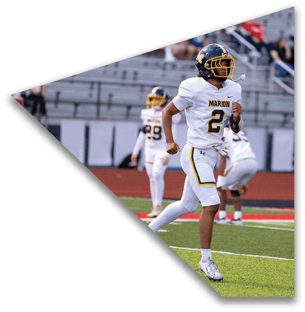 A person wearing a white football uniform with the number 2 and a helmet is running on a football field with other players and empty bleachers in the background. Description generated by AI