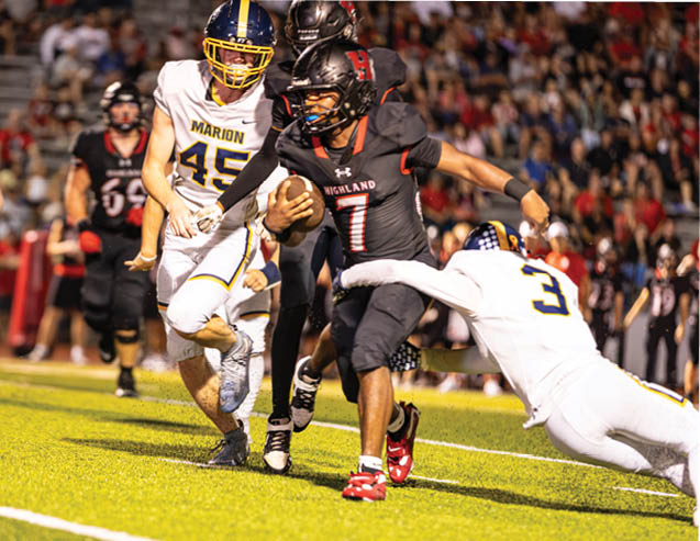 A person in a black football uniform with the number 7 is running with the ball while being tackled by a person in a white uniform and pursued by others on a football field. Description generated by AI