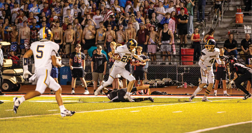 People in football uniforms are actively playing on a field with a crowd of spectators in the background. Description generated by AI