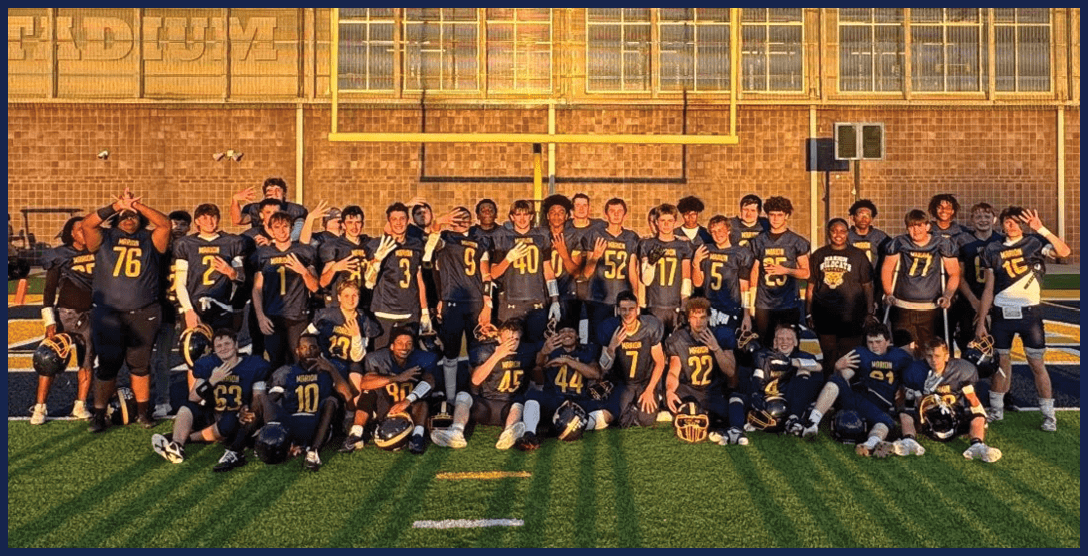 A group of people wearing dark sports jerseys with numbers pose together on a football field under a goalpost. Description generated by AI