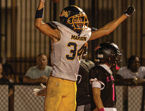A person in yellow sports gear jumps to catch a football in the end zone while two other players and a referee watch during a nighttime game. Description generated by AI