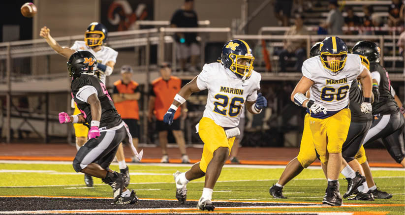 Several people in football uniforms are actively playing on a field with one person running while others are positioned around them. Description generated by AI