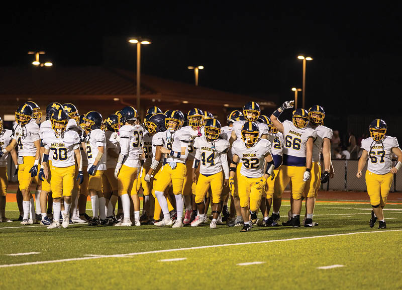 A group of people wearing yellow pants and white jerseys with helmets are gathered on a football field at night. Description generated by AI