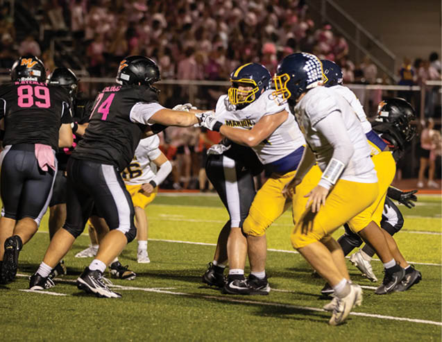 Several people wearing football uniforms are engaged in a play on a well-lit field with a crowd in the background. Description generated by AI