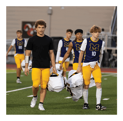 People wearing yellow and white sports uniforms are walking on a grassy field carrying helmets. Description generated by AI