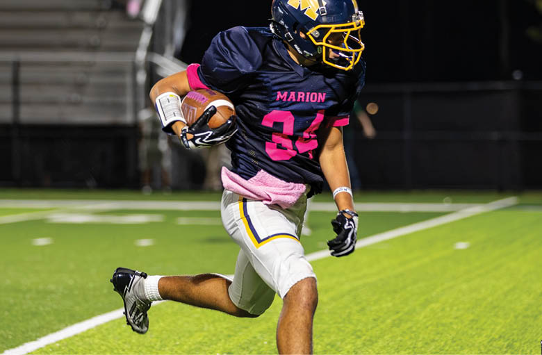 A person wearing a sports uniform with the number 34 is running on a football field while holding a football. Description generated by AI