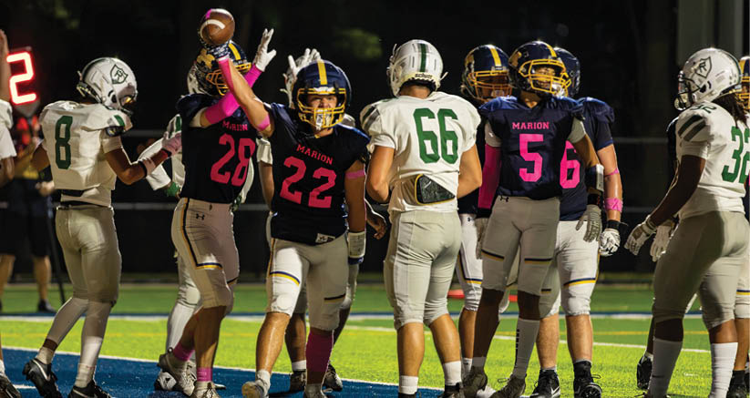 People wearing football uniforms are gathered on a field, with some celebrating and others standing nearby. Description generated by AI
