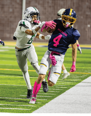 People in football uniforms are actively playing on a field with one person running near the sideline while others chase behind. Description generated by AI