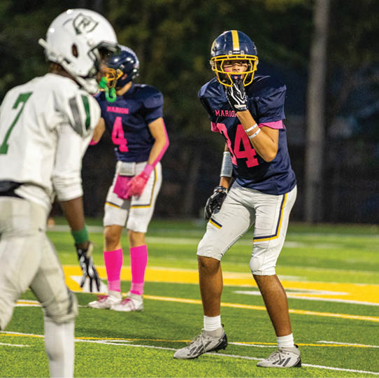 A person wearing a navy blue football jersey with the number 44 and white football pants is standing on a green and yellow football field. Description generated by AI