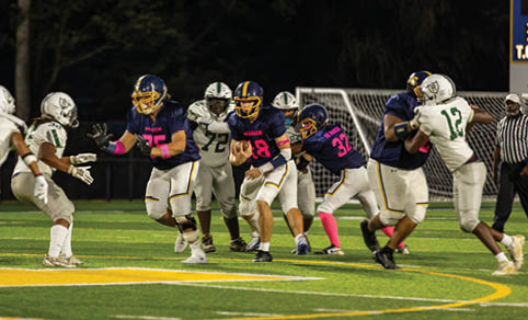 People wearing football uniforms are actively playing on a field under stadium lights during a nighttime game. Description generated by AI