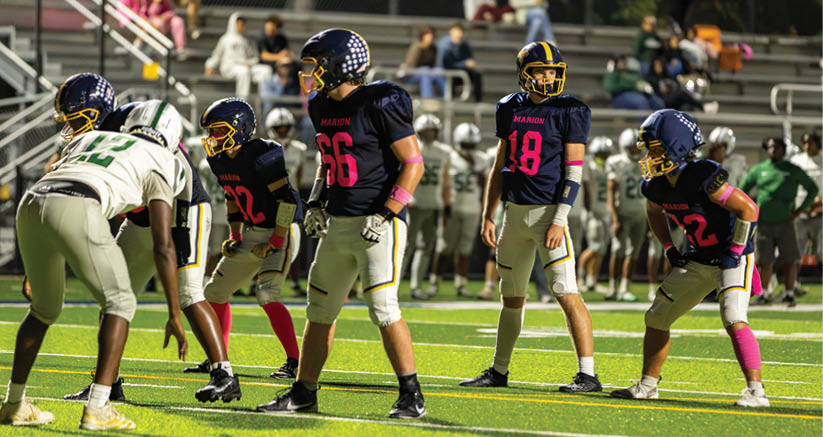 A group of people wearing football helmets and uniforms are positioned on a field, preparing for a play during a game. Description generated by AI