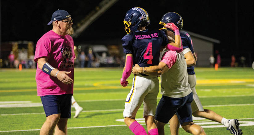 People on a football field are interacting, with one person in a football uniform being supported by two others wearing casual athletic clothing. Description generated by AI
