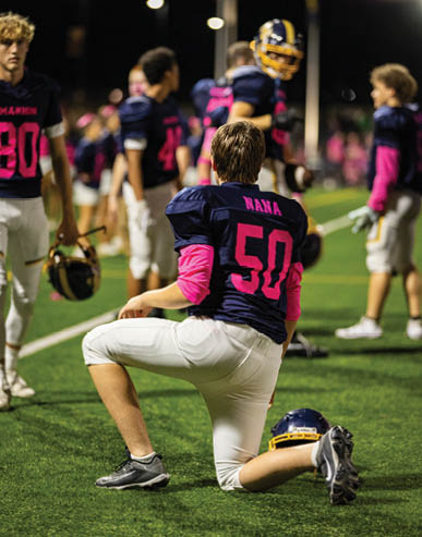 People wearing football uniforms are gathered on a field at night, with one person holding a football and others standing nearby. Description generated by AI