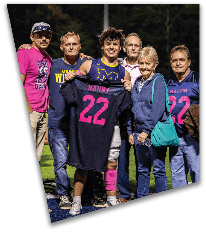 A group of six adults standing closely together outdoors at night, smiling, with one person in the center holding a sports jersey. Description generated by AI