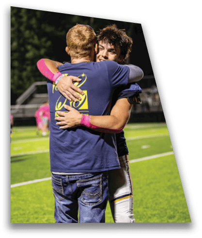 Two people embrace on a sports field at night while another person stands nearby watching. Description generated by AI