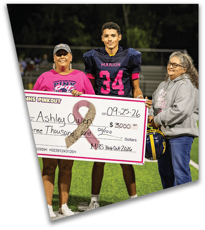 Three people stand on a sports field holding a large ceremonial check for a breast cancer fundraiser event dated 09-25-26. Description generated by AI