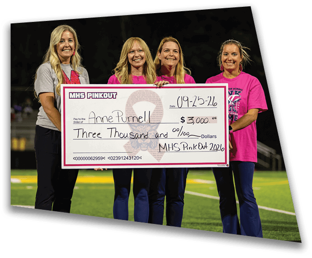 Four adults standing on a sports field holding a large check for a fundraising event called MHS PinkOut dated 09-25-26. Description generated by AI