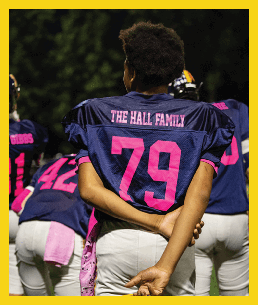A person wearing a dark blue sports jersey with pink text reading “THE HALL FAMILY" and the number 70 on the back is standing outdoors. Description generated by AI