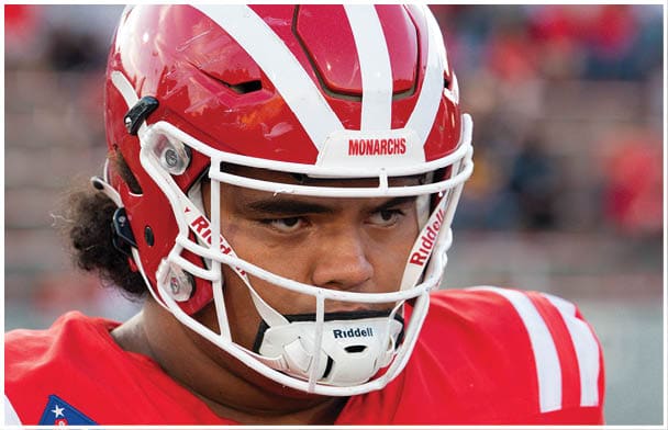 A person wearing a red football helmet and red jersey with white stripes is looking to the side. Description generated by AI