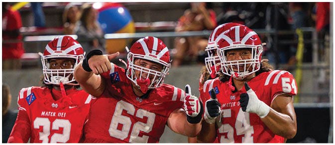 Three people in red football uniforms with helmets are posing on a field, two giving thumbs up and one pointing forward. Description generated by AI