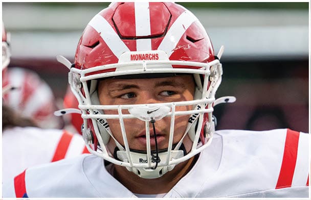 A person wearing a red and white helmet is standing outdoors with a blurred natural background. Description generated by AI