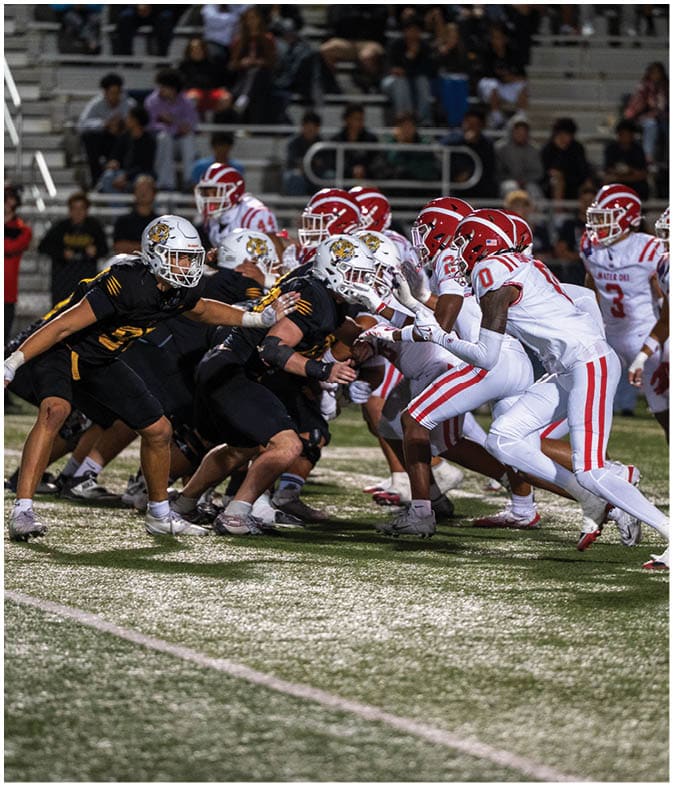 Two opposing American football teams in black and white uniforms are lined up facing each other on a field during a game. Description generated by AI