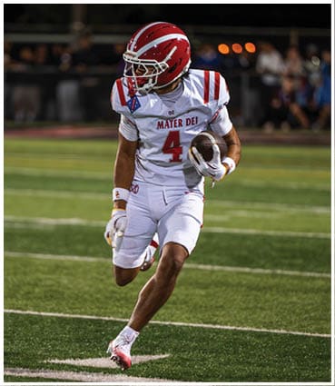 A person wearing a white football uniform with red accents and the number 4 is running on a football field while holding a football. Description generated by AI