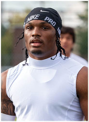 A person wearing a black Nike headband and a white sleeveless athletic shirt is looking slightly off-camera with a neutral expression. Description generated by AI
