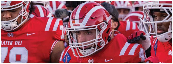 A group of people wearing red and white football helmets are gathered closely together, likely preparing for a game or practice. Description generated by AI
