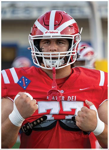 A person wearing a red football uniform and helmet with the number 77 on the jersey is clenching their fists in a determined pose. Description generated by AI
