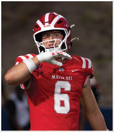 A person wearing a red and white football uniform and helmet is preparing to throw a football. Description generated by AI