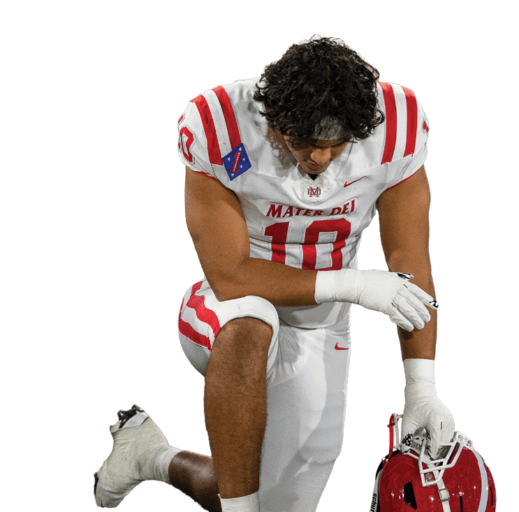 A person wearing a white and red sports uniform is kneeling while holding a red football helmet. Description generated by AI