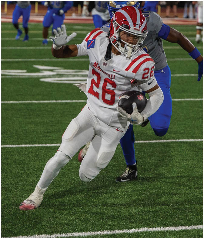 A person in a white and red football uniform is running with the ball while being closely pursued by a person in a blue and gray uniform on a football field at night. Description generated by AI
