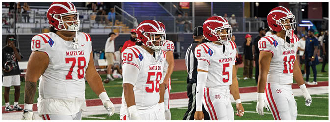 Four people wearing white sports uniforms with red stripes and white cleats are walking on a green football field. Description generated by AI