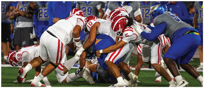 A group of people in football uniforms are engaged in a play on the field with some players in white and red and others in blue and gray. Description generated by AI