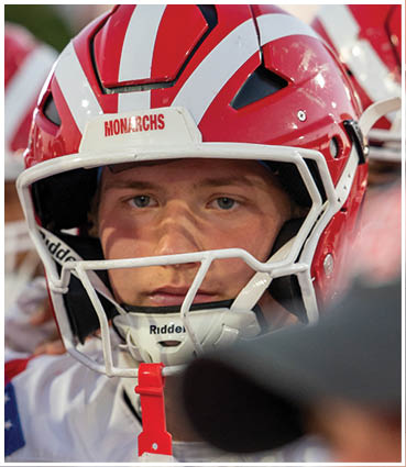 A person wearing a red and white football helmet with the word “MONARCHS" partially visible on the front. Description generated by AI