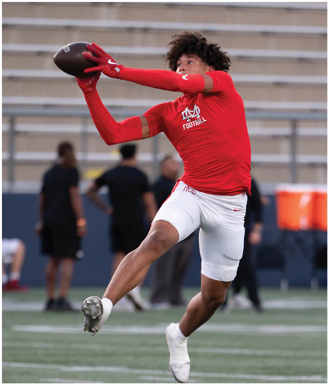 A person wearing a red long-sleeve shirt and gloves is reaching out to catch a football in an outdoor stadium. Description generated by AI