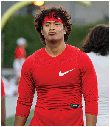 A person wearing a red athletic outfit and headband is standing on a sports field with a goalpost in the background. Description generated by AI