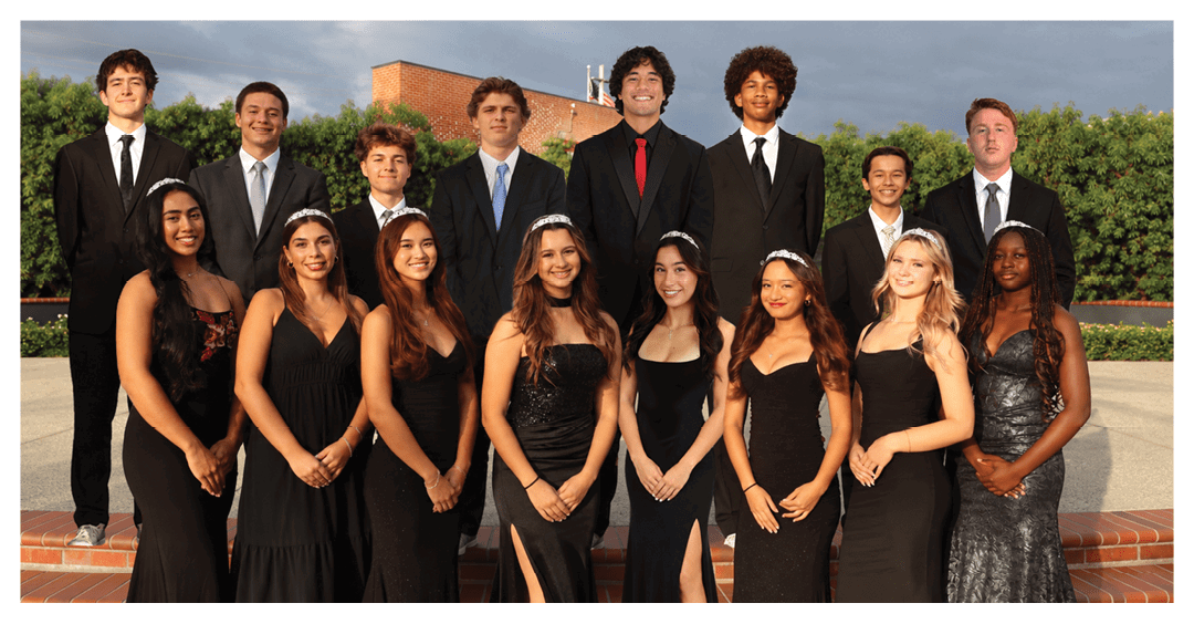 A group of formally dressed adults wearing suits and elegant black dresses pose together outdoors on steps with greenery and a building in the background. Description generated by AI