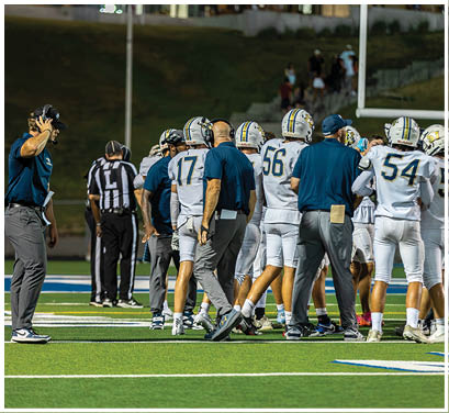 A group of football players huddled together on the field. Description generated by AI