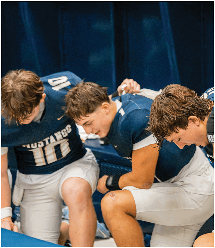 Three football players in blue and white uniforms running on a field. Description generated by AI