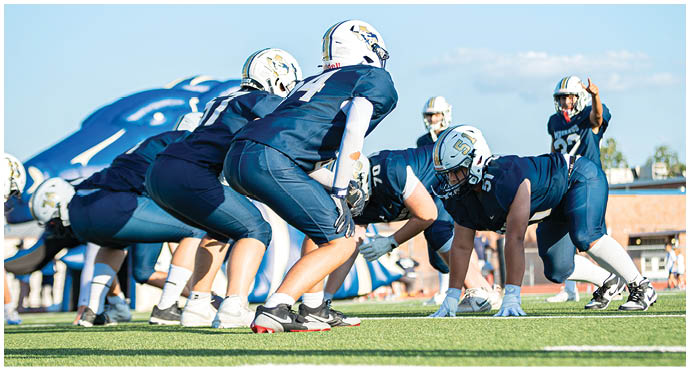 Three football players in blue and white uniforms running on a field. Description generated by AI