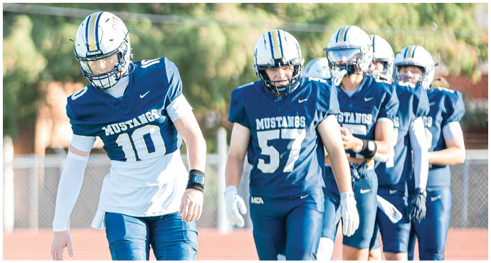 Three football players in blue and white uniforms running on a field. Description generated by AI