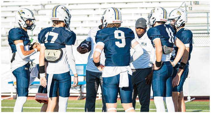 Three football players in blue and white uniforms running on a field. Description generated by AI