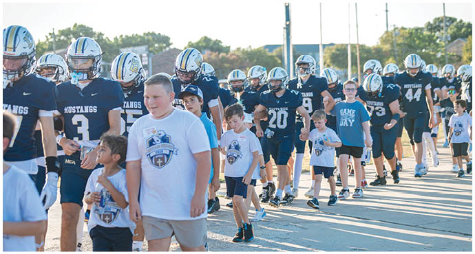 Three football players in blue and white uniforms running on a field. Description generated by AI