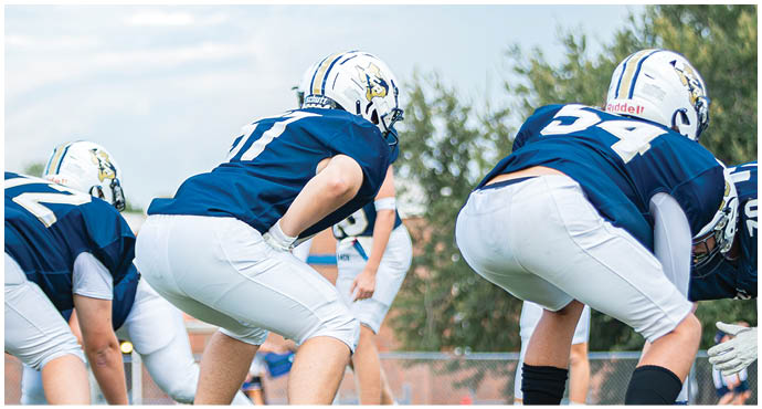 Three football players in blue and white uniforms running on a field. Description generated by AI