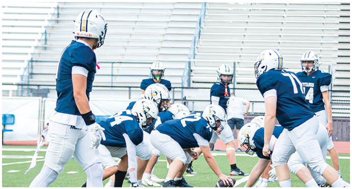 Three football players in blue and white uniforms running on a field. Description generated by AI