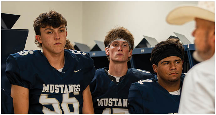 Three football players in blue and white uniforms running on a field. Description generated by AI