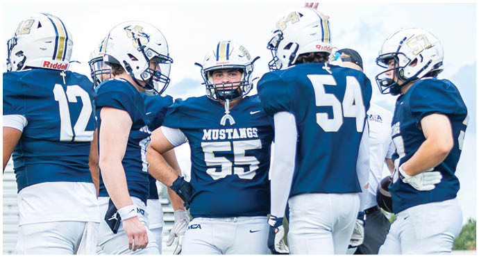 Three football players in blue and white uniforms running on a field. Description generated by AI